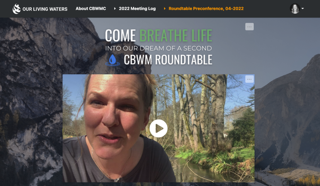 **Alt Text:** A woman is speaking in a video thumbnail, set against a lush background of trees and a gently flowing stream. Above her, text reads, Come Breathe Life into Our Dream of a Second CBWM Roundtable. The surrounding webpage is framed by picturesque mountain scenery, giving an inspiring and natural feel to the content. / **Translation in Canadian French:** Une femme parle dans la miniature dune vidéo, se tenant devant un arrière-plan verdoyant composé darbres et dun ruisseau coulant doucement. Au-dessus delle, le texte dit : Venez insuffler de la vie à notre rêve dune deuxième Table Ronde sur les BVCM. La page Web est encadrée par des paysages montagneux pittoresques qui confèrent une sensation inspirante et naturelle au contenu.